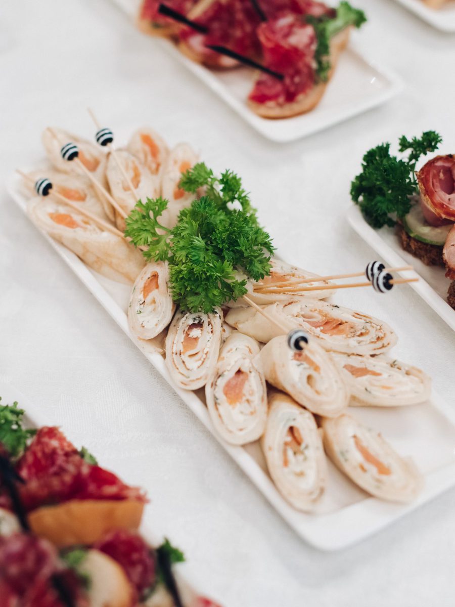 Close-up of tasty fresh fish rolls with cream cheese and parsley and canape with red caviar and salmon with greens served on white rectangular plates on wedding party birthday corporate party dining event.
